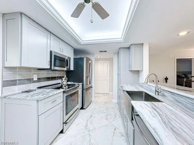Kitchen with appliances with stainless steel finishes, light stone countertops, tasteful backsplash, light marble finish flooring, and a raised ceiling