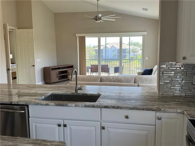 Kitchen featuring stainless steel dishwasher, stone counters, a ceiling fan, visible vents, and a sink