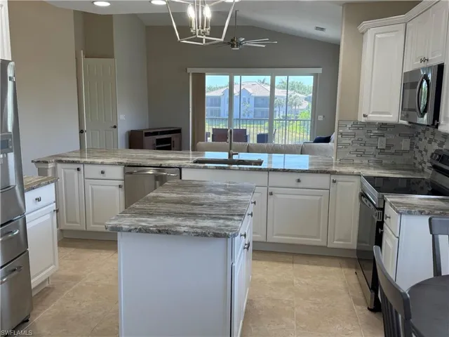 Kitchen with lofted ceiling, a center island, decorative backsplash, stainless steel appliances, and a sink