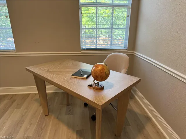 Office area featuring light wood-style floors, a textured wall, healthy amount of natural light, and baseboards