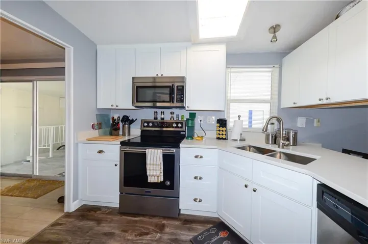 Kitchen featuring white cabinets, appliances with stainless steel finishes, light stone countertops, and dark wood-style flooring