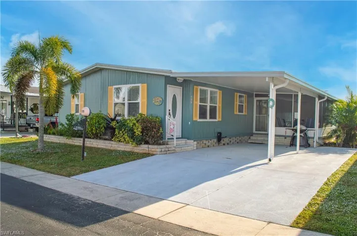 Manufactured / mobile home featuring an attached carport, entry steps, concrete driveway, and a front lawn