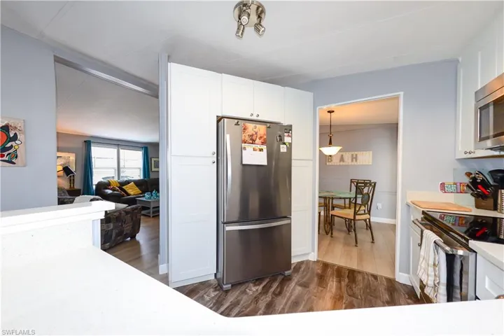 Kitchen with stainless steel appliances, white cabinetry, dark wood finished floors, light stone counters, and decorative light fixtures