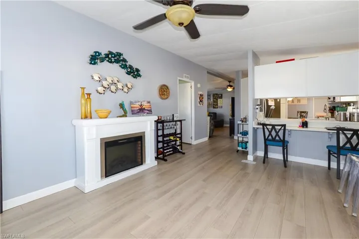 Living room with a glass covered fireplace, ceiling fan, and light wood-style flooring
