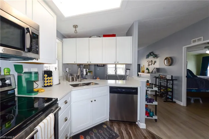 Kitchen featuring stainless steel appliances, white cabinetry, dark wood-type flooring, and light stone counters