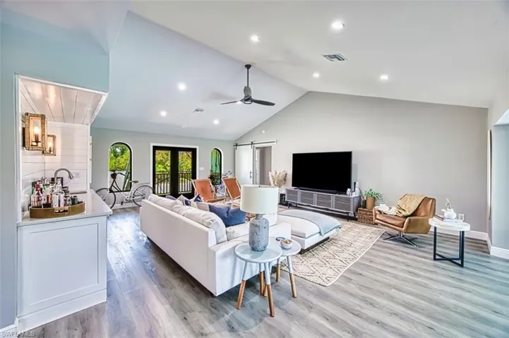 Living area featuring vaulted ceiling, light wood-style flooring, ceiling fan, a barn door, and baseboards