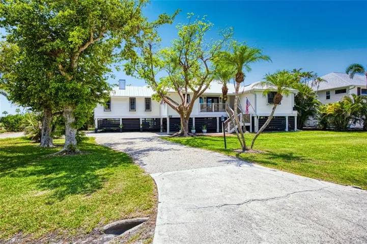 Beach home with driveway, stairs, and a front lawn