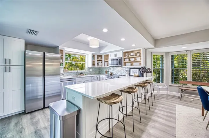 Kitchen with appliances with stainless steel finishes, open shelves, a peninsula, and light quartz countertops