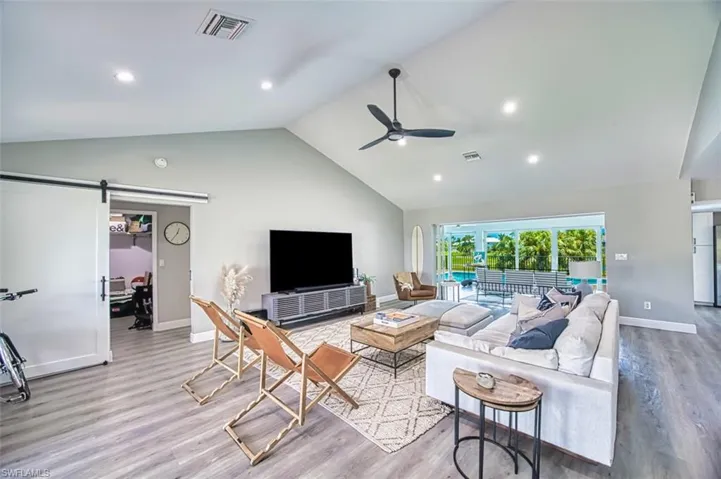 Living area featuring a barn door, high vaulted ceiling, wood like finished floors, relaxing decor