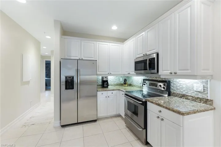 Kitchen with white cabinets, backsplash, appliances with stainless steel finishes, and light tile patterned flooring