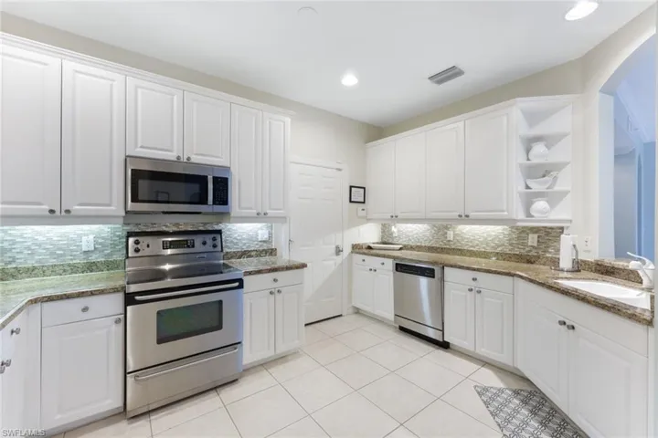 Kitchen featuring light tile patterned flooring, sink, white cabinetry, stainless steel appliances, and backsplash