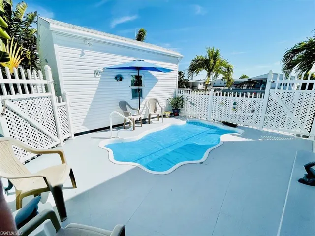 Private outdoor area featuring a freeform swimming pool with safety cover, white picket fencing, and a painted concrete patio