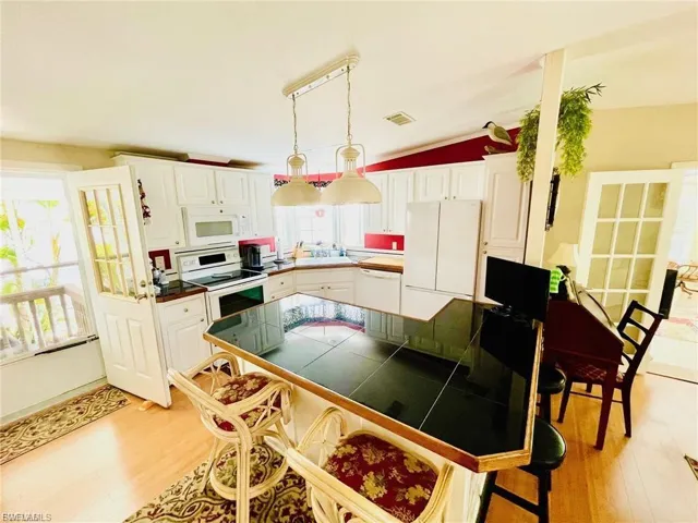 Kitchen featuring white cabinetry, solid bamboo wood flooring, a black tile-top island, stainless steel appliances, and French doors to the left leading to the family room.