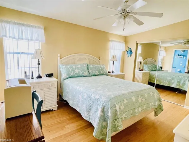 Bedroom featuring solid bamboo wood flooring, a white ceiling fan, and mirrored closet doors