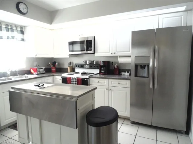 Kitchen featuring stainless steel appliances, white cabinetry, dark countertops, and light tile patterned flooring