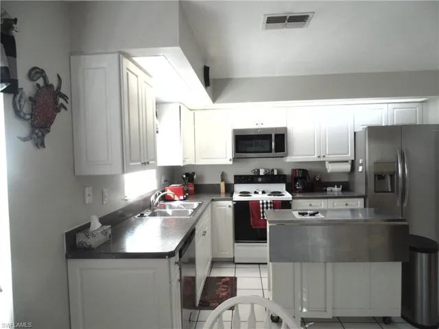 Kitchen with appliances with stainless steel finishes, white cabinetry, dark countertops, and light tile patterned floors