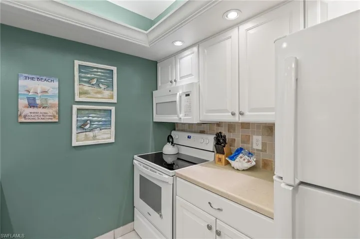 Kitchen with white appliances, backsplash, recessed lighting, white cabinetry, and light countertops