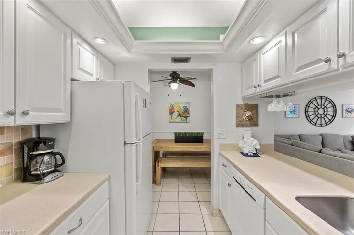 Kitchen with decorative backsplash, a raised ceiling, white appliances, and white cabinetry