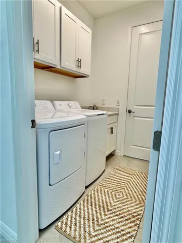 Laundry area featuring cabinet space, independent washer and dryer, and light tile patterned flooring with utility sink