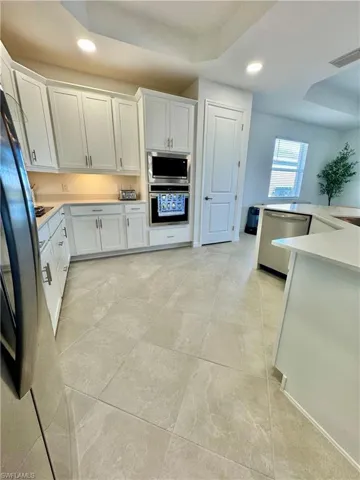 Kitchen with recessed lighting, a raised ceiling, white cabinets, stainless steel appliances, and light stone countertops
