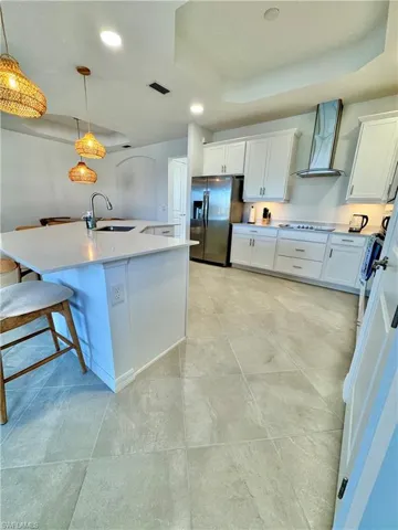 Kitchen with a raised ceiling, recessed lighting, white cabinets, stainless steel fridge with ice dispenser, and pendant lighting