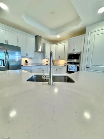 Kitchen with recessed lighting, a raised ceiling, white cabinetry, stainless steel appliances, and light stone countertops