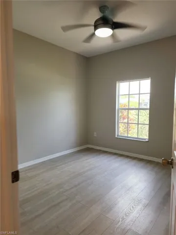 Neutral-toned room featuring a ceiling fan with integrated lighting, a large window, and light wood-finish flooring