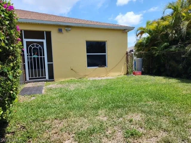Grassy backyard featuring a perimeter chain-link fence, mature foliage, and a security screen door