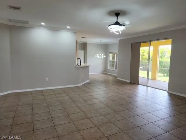 Open concept living space featuring neutral tone tile flooring and crown molding
