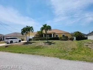 Single-story residence featuring a warm yellow exterior with a matching tile roof, a two-car garage, mature palm trees, and a concrete driveway