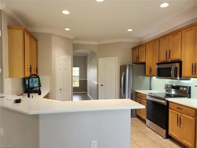 Kitchen featuring light wood cabinetry, stainless steel appliances, recessed lighting, and a breakfast bar with solid surface countertops