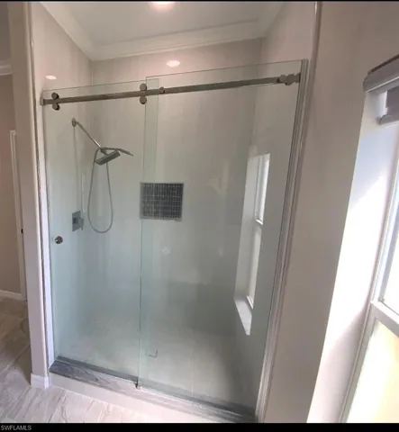 Glass-enclosed shower featuring a sliding door, rain showerhead, handheld shower, and an integrated tiled niche