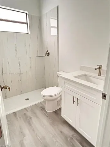 Bathroom with tiled shower, vanity, hardwood / wood-style flooring, and toilet