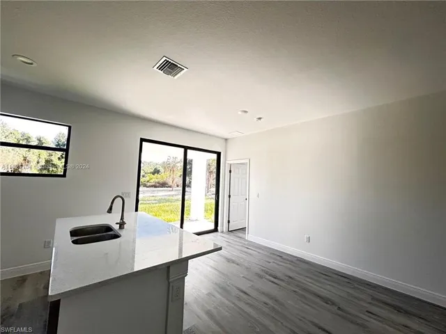 Kitchen with sink, hardwood / wood-style flooring, a kitchen island with sink, and light stone counters