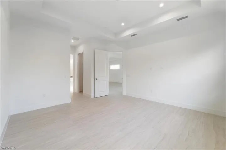 Empty room with light wood-style floors, a raised ceiling, recessed lighting, and visible vents