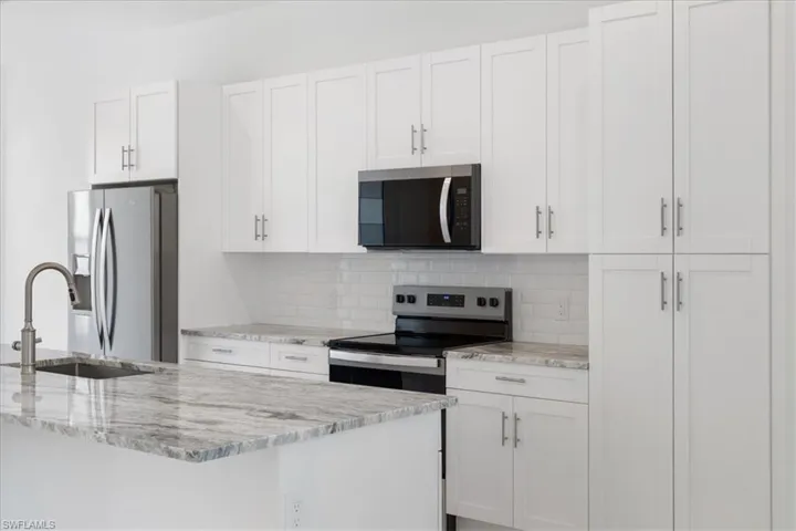 Kitchen with appliances with stainless steel finishes, tasteful backsplash, light stone countertops, a sink, and white cabinets
