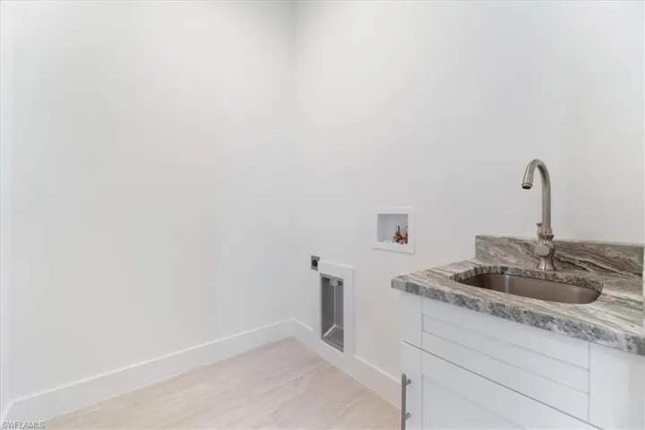 Clothes washing area featuring cabinet space, a sink, hookup for a washing machine, electric dryer hookup, and baseboards