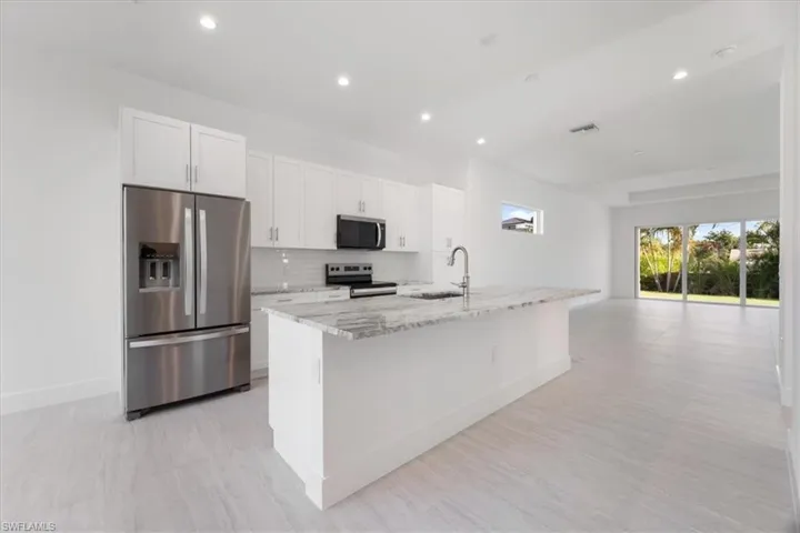 Kitchen with backsplash, light stone countertops, a sink, white cabinets, and stainless steel appliances