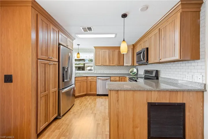 Kitchen with hanging light fixtures, a peninsula, stainless steel appliances, light stone counters, and light wood finished floors
