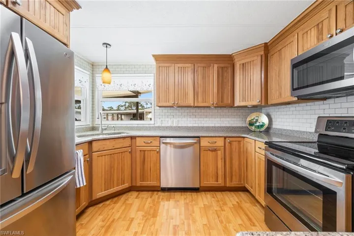 Kitchen featuring stainless steel appliances, pendant lighting, light stone countertops, light wood-style floors, and tasteful backsplash