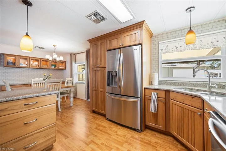 Kitchen with stainless steel appliances, light stone counters, wood finish cabinets, light wood finished floors, and tasteful backsplash