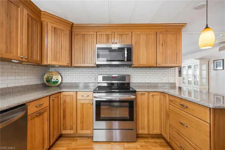 Kitchen featuring stainless steel appliances, wood finish cabinets, light wood-style floors, light stone countertops, and a peninsula