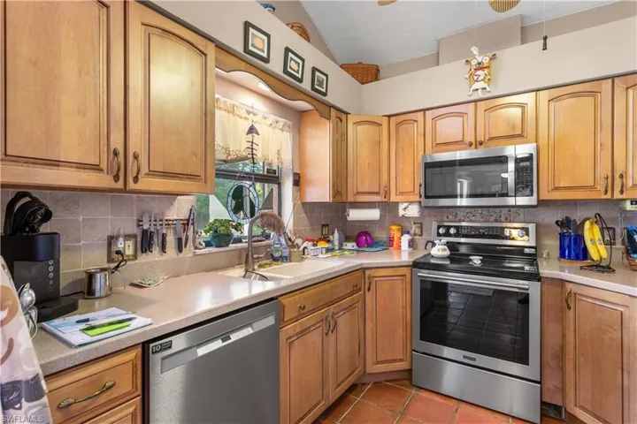 Kitchen with stainless steel appliances, vaulted ceiling, tile floors, and backsplash