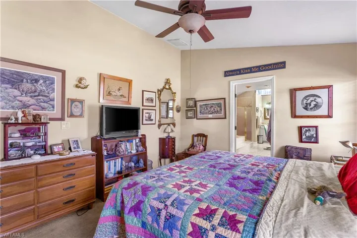 Bedroom featuring ensuite bath, ceiling fan, lofted ceiling, and light carpet