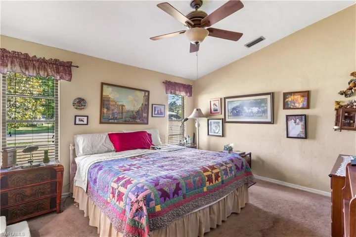 Bedroom with vaulted ceiling, carpet, ceiling fan, and multiple windows