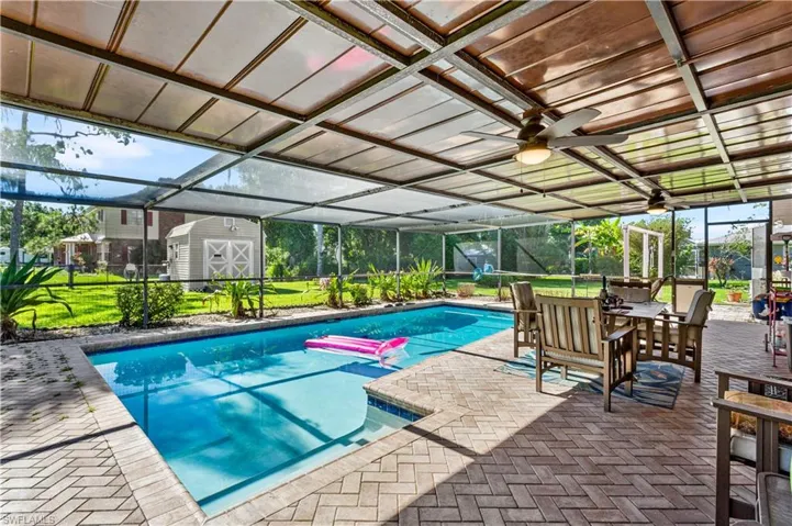 View of swimming pool featuring a patio area, glass enclosure, ceiling fan, and a storage shed