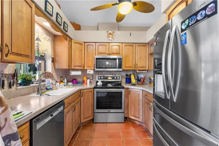 Kitchen with appliances with stainless steel finishes, sink, tasteful backsplash, ceiling fan, and light tile floors
