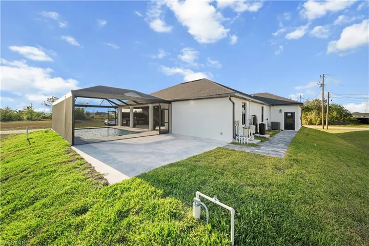 View of front of property with an outdoor pool, a patio, glass enclosure, a front yard, and stucco siding