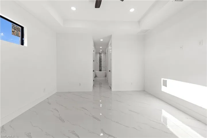 Empty room featuring baseboards, marble finish floor, ceiling fan, recessed lighting, and a tray ceiling