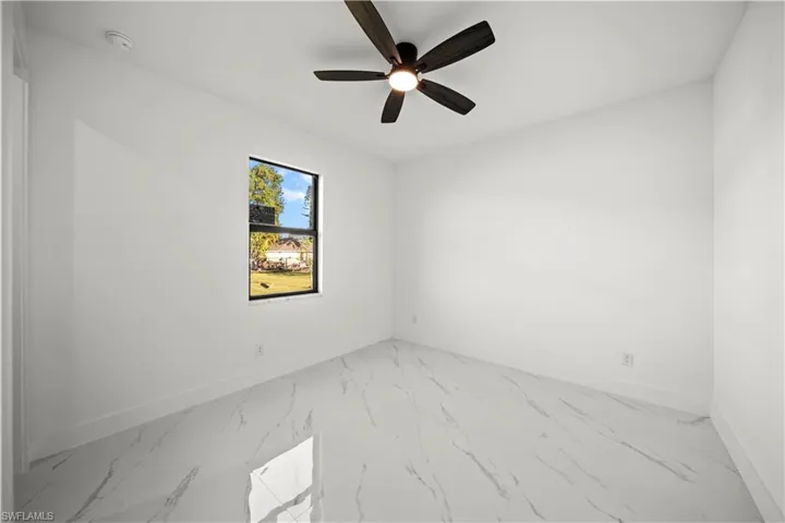 Empty room featuring marble finish floor, baseboards, and ceiling fan
